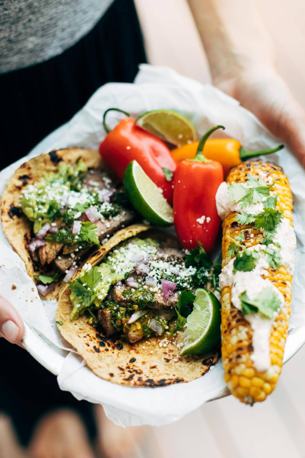 Plate with tacos, grilled corn on the cob, and veggies.