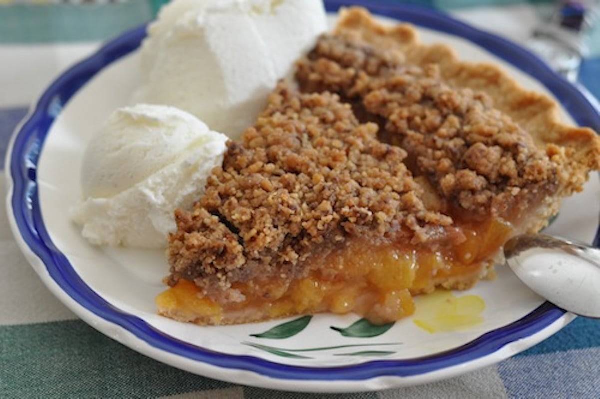 Classic peach pie on a plate with vanilla ice cream.